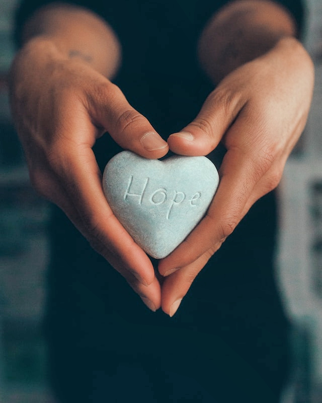 Not By Sight Media - Podcasts to give you hope - Person's hands holding a heart-shaped rock with the word "hope" engraved on it.